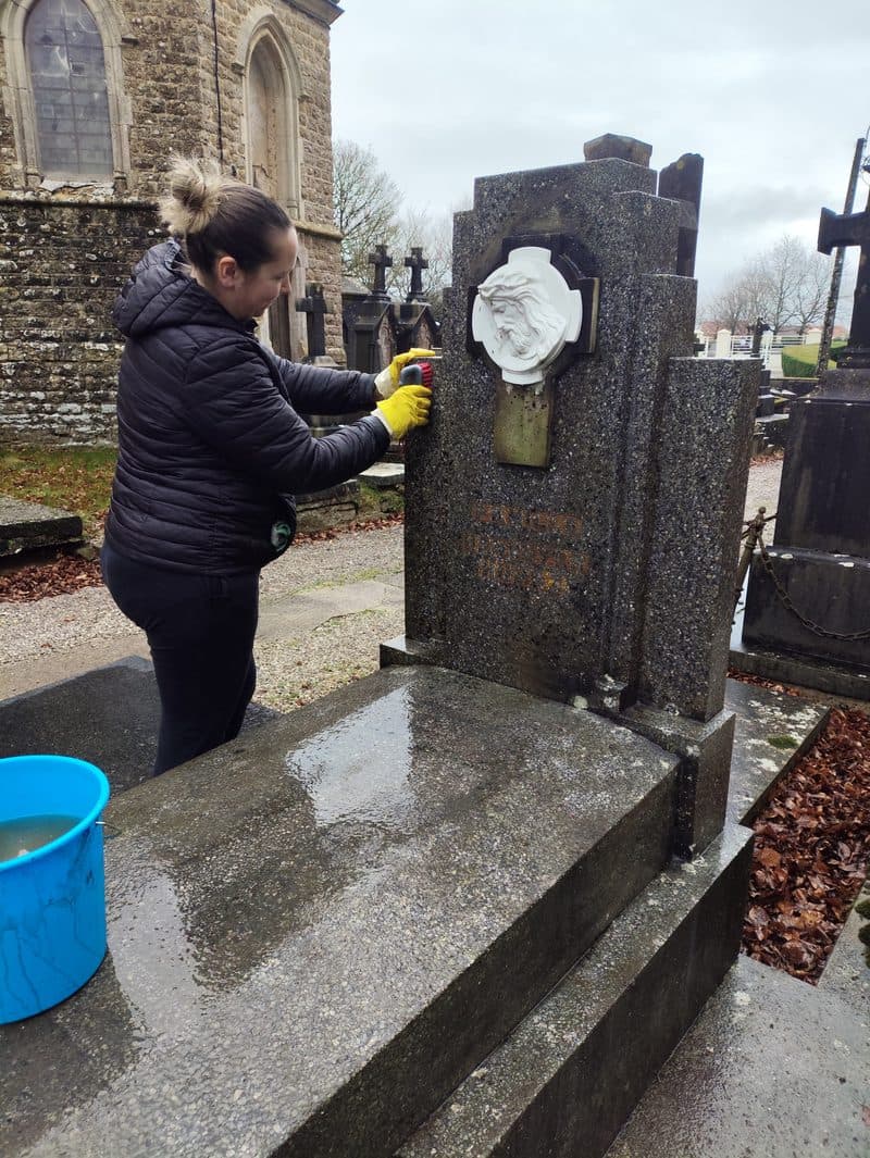 Sophie brosse la stèle, gants jaunes, un seau d’eau posé sur la dalle.