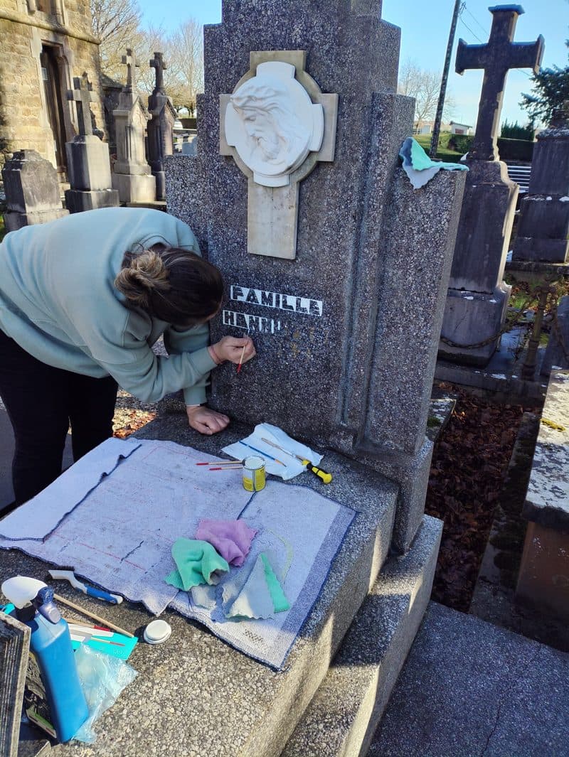 Sophie repeint au pinceau les lettres gravées de la stèle.