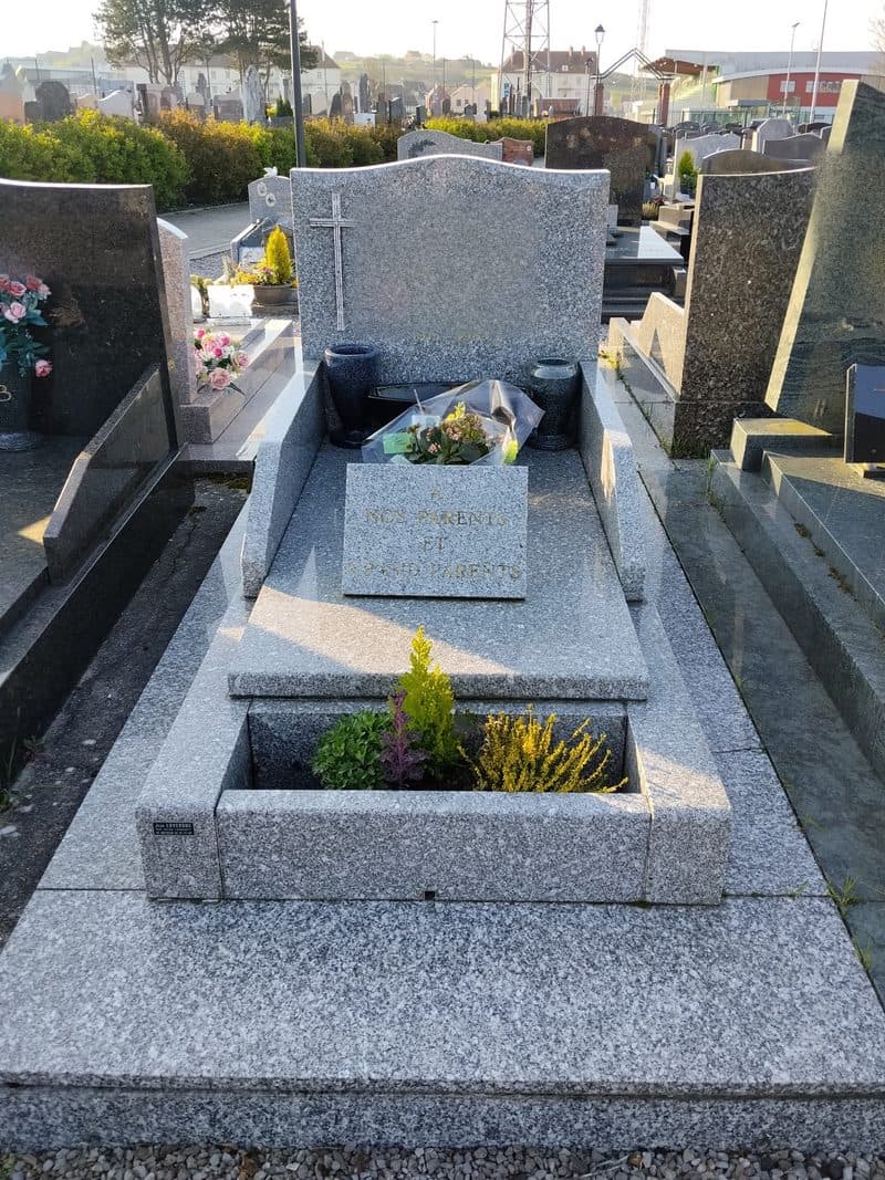 Une tombe en granit gris, propre, le bac fleuri de bruyères.