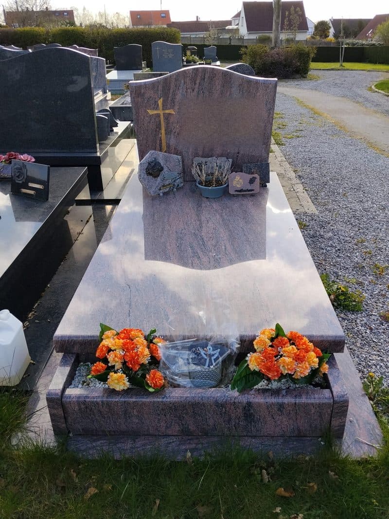 Une tombe en granit rose, la dalle lustrée, deux bouquets orange.
