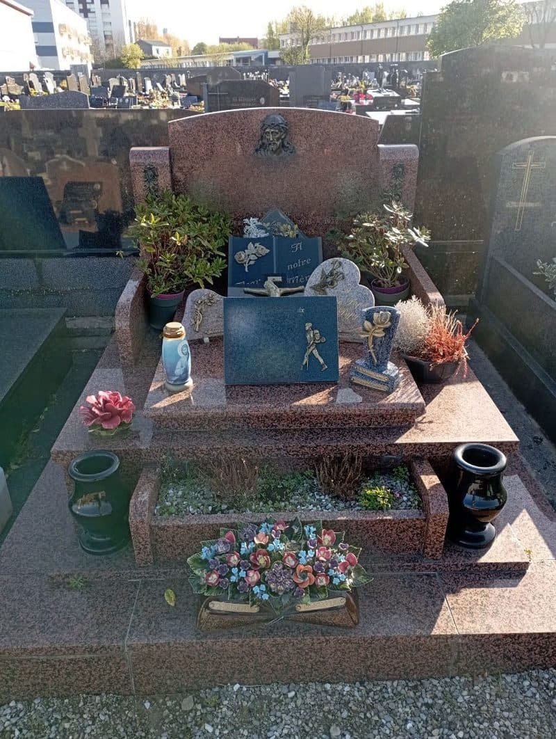 Une tombe en marbre rose, entretenue et fleurie, avec ses plaques.