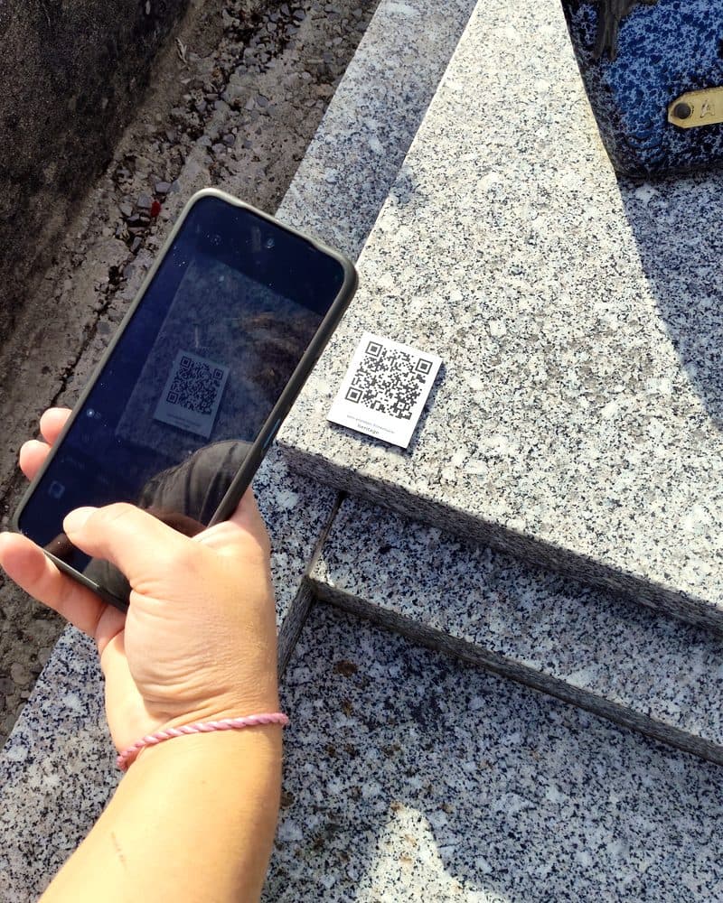 Une main tient un téléphone qui scanne le QR code de la plaque.